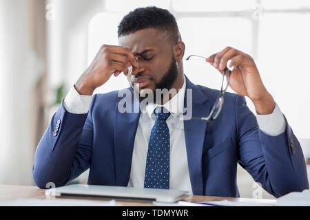 Frustrated african businessman massaging his nose in office Stock Photo