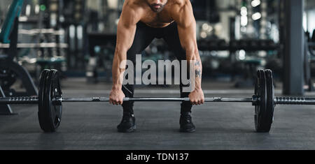 Muscular guy lifting heavy barbell from gym floor Stock Photo