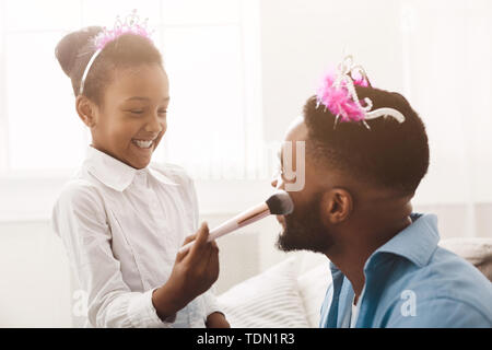 Little Daughter Doing Makeup To Her Dad, Wearing Crowns Stock Photo