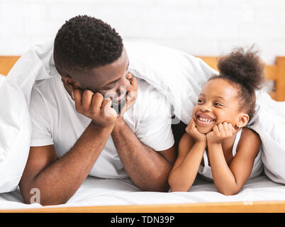 Cute african dad and daughter lying on bed and smiling to each other Stock Photo