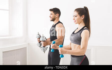 Concentrated couple doing exercise with dumbbells in studio Stock Photo