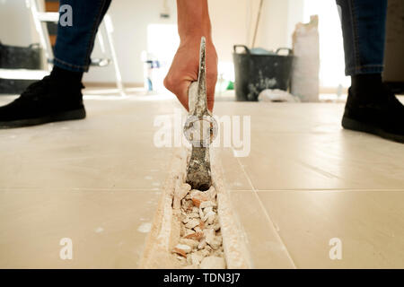 closeup of caucasian man making a groove in a tiled floor using a pickaxe Stock Photo
