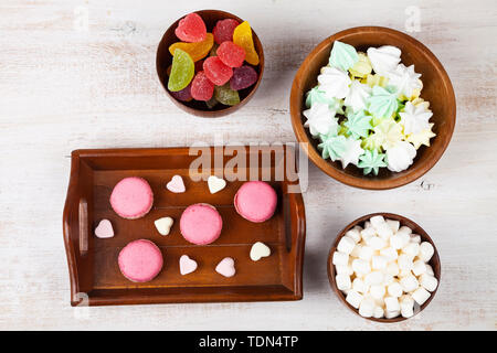 Strawberry macarons, marmalade,meringues and marshmallows in bowls and a tray on a wooden background, top view. Stock Photo