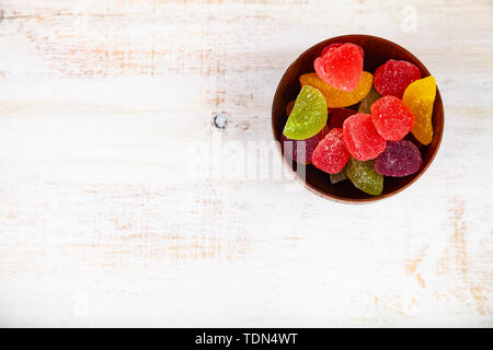 Multicolored marmalade in a bowl on a wooden background, top view. Delicious dessert. Stock Photo