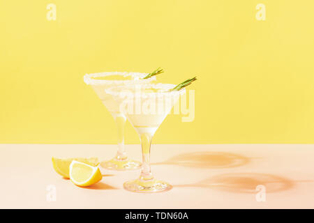 Lemon lemonade drink in elegant glasses on a bright pastel colored background. Bright sunshine. Summer concept. Stock Photo