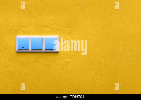 Blue switches on a yellow concrete wall. Colorful electrical switch. Creative style Stock Photo