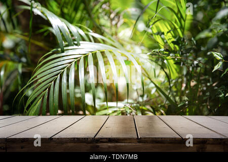 Dark wood table top (Bar) with blur on green palm leaves or tree in tropical forest with bokeh light at background - Using for Mock up template for di Stock Photo