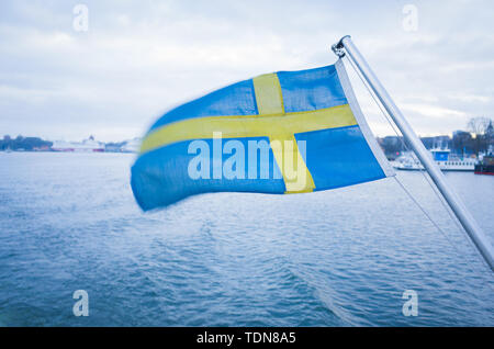 Swedish national flag flutters in the wind at the stern of a ferry navigating the Stockholm archipelago on an overcast winter's day. Stock Photo