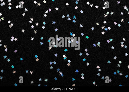 Iridescent Silver stars confetti on black. Festive holiday background. Glowing stars sparkles. Celebration concept, flat lay. Stock Photo