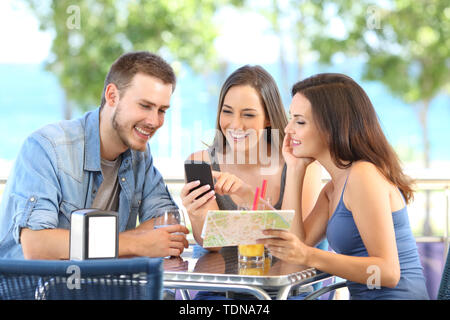 Group of tourists checking smart phone and map on vacation in a coffee shop or hotel on the beach Stock Photo