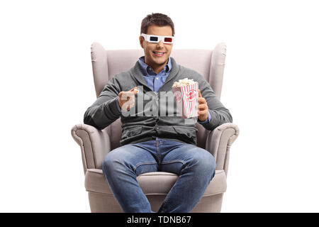 Young man wearing 3D glasses sitting in an armchair and eating popcorn isolated on white background Stock Photo