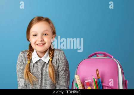 Closeup portrait of little girl schoolgirl with backpack on blue background. Back to school. The concept of education. Stock Photo