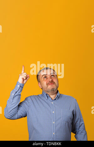 Handsome bearded man in a shirt, points his finger in upwards on a yellow background. Copy space Stock Photo