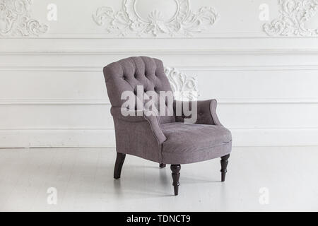 Living room in the Rococo style. Vintage grey armchair against the wall with plaster stucco patterns. Selective focus Stock Photo
