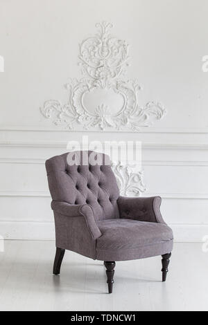 Living room in the Rococo style. Vintage grey armchair against the wall with plaster stucco patterns. Selective focus Stock Photo