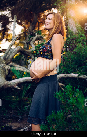 Young pregnant woman with her belly up in the air, posing carefree in the woods. Stock Photo