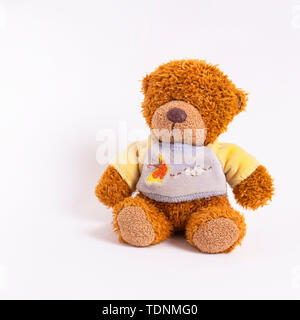 A small teddy bear in a yellow-blue sweater sits on a white background Stock Photo