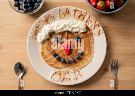 Sweet crepe decorated with whipped cream and berries in shape of funny face with happy fathers day inscription, gift for daddy Stock Photo