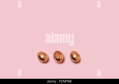 Three decorated with gold Easter eggs on a pink background. Top view, copy space for text for banner, poster, website. Stock Photo