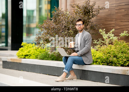 Young pensive author in smart casual having drink while thinking of new ideas for new book in urban environment Stock Photo