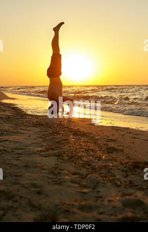Young man practice balance asana on summer yoga session on beautiful golden beach of tropical island. Guy doing Salamba Sirsasana supported headstand Stock Photo