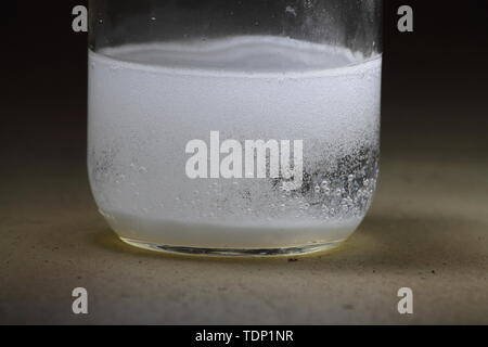 Closeup of a vinegar and baking soda reaction happening in the bottom of a glass jar; vinegar clearing of bubbles Stock Photo