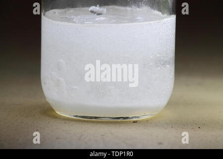 Closeup of a vinegar and baking soda reaction happening in the bottom of a glass jar; solution cloudy Stock Photo