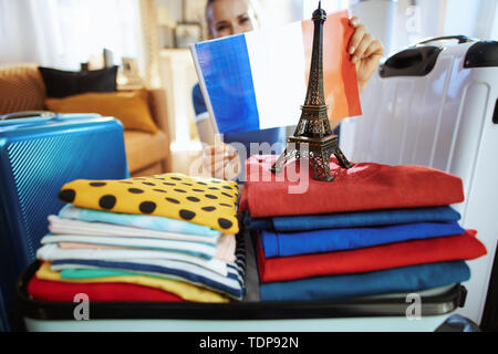 Closeup on happy modern traveller woman in blue t-shirt at modern home in sunny summer day showing French flag and Eiffel tower souvenir. Stock Photo