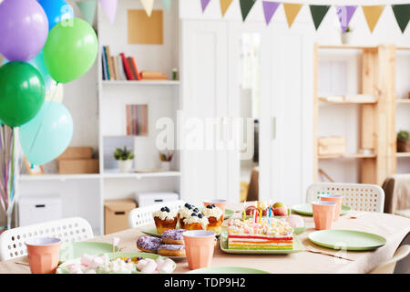 Background image of dinner table set with sweets and cake for Birthday party in decorated room, copy space Stock Photo