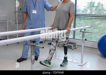 Male physiotherapist helping patient walking with parallel bars in the hospital Stock Photo