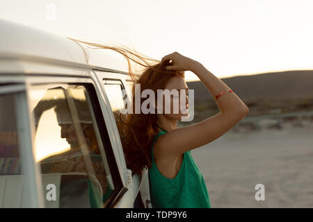 Beautiful woman with eyes closed leaning on camper van at beach