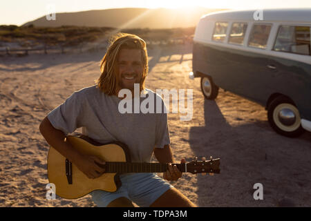 Happy young man playing guitar near camper van at beach Stock Photo