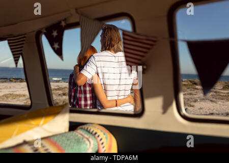 Couple with arms around standing together near camper van at beach Stock Photo
