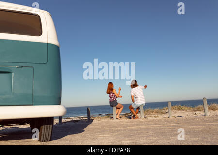 Young couple sitting together on bollard at beach Stock Photo