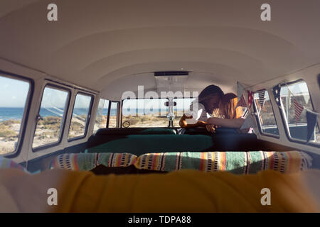 Young couple kissing each other in front seat of camper van at beach Stock Photo