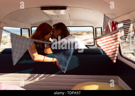 Young couple kissing each other in front seat of camper van at beach Stock Photo