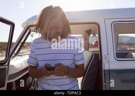 Young man using mobile phone near van at beach Stock Photo