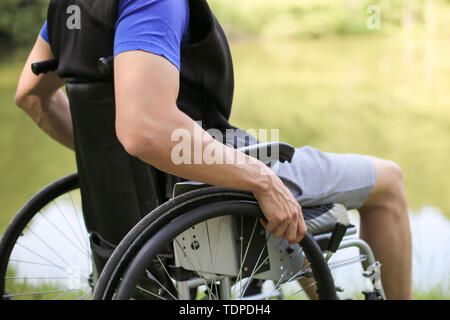 Happy and young disabled or handicapped man sitting on a wheelchair in nature. Stock Photo