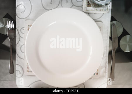 A top down shot looking down at a white plate next to silver knife and fork at an empty seat Stock Photo