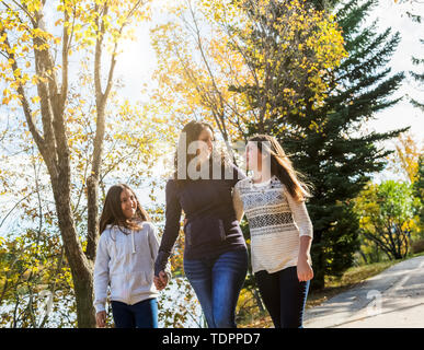 A mother and her two daughters walking and talking on a pathway in a city park on a warm autumn day; Edmonton, Alberta, Canada Stock Photo