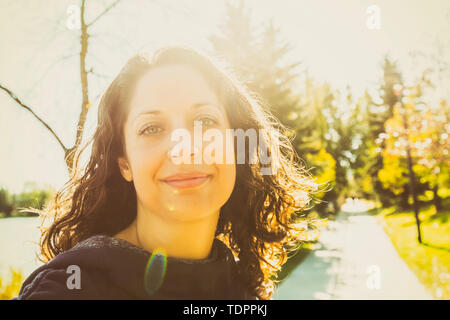 A women stopping to pose for the camera while walking on a path beside a lake in a city park on a warm fall day; Edmonton, Alberta, Canada Stock Photo