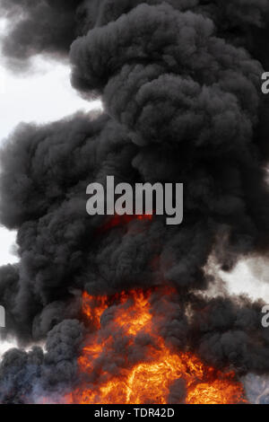 Huge flames of red-orange fire and motion clouds of black smoke covered sky. Motion blur from strong fire and high temperature from flames. Stock Photo