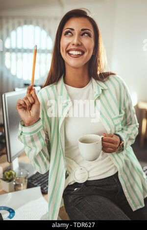 A young successful business woman enjoys her success, drinks coffee in the office and thinking something nice. Stock Photo