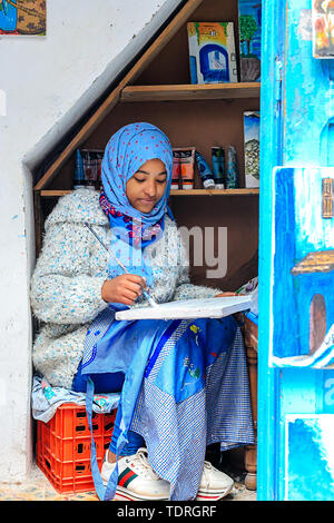 A beautiful Moroccan girl, a Muslim, street artist paints a picture with a brush in a small workshop. Chefchaouen, Morocco, Africa Stock Photo