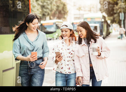 Happy Asian girls using mobile phone outdoor - Young millennial people having fun with new smartphone app technology Stock Photo