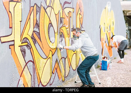 Graffiti artists painting colorful mural on a grey wall - Creative men performing drawing murals Stock Photo