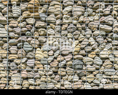 gabion wall pattern. metal grid with many round natural stones inside Stock Photo