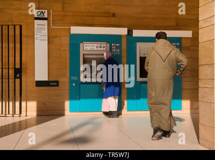 woman with headscarf and man at an automatic cash dispensers, Morocco, Quarzazate Stock Photo