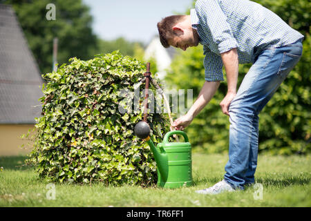 young man filling water in a watering can in the garden, Germany Stock Photo