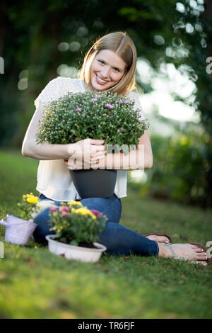 young blond woman sitting in a meadow with an aster in the arm , Germany Stock Photo